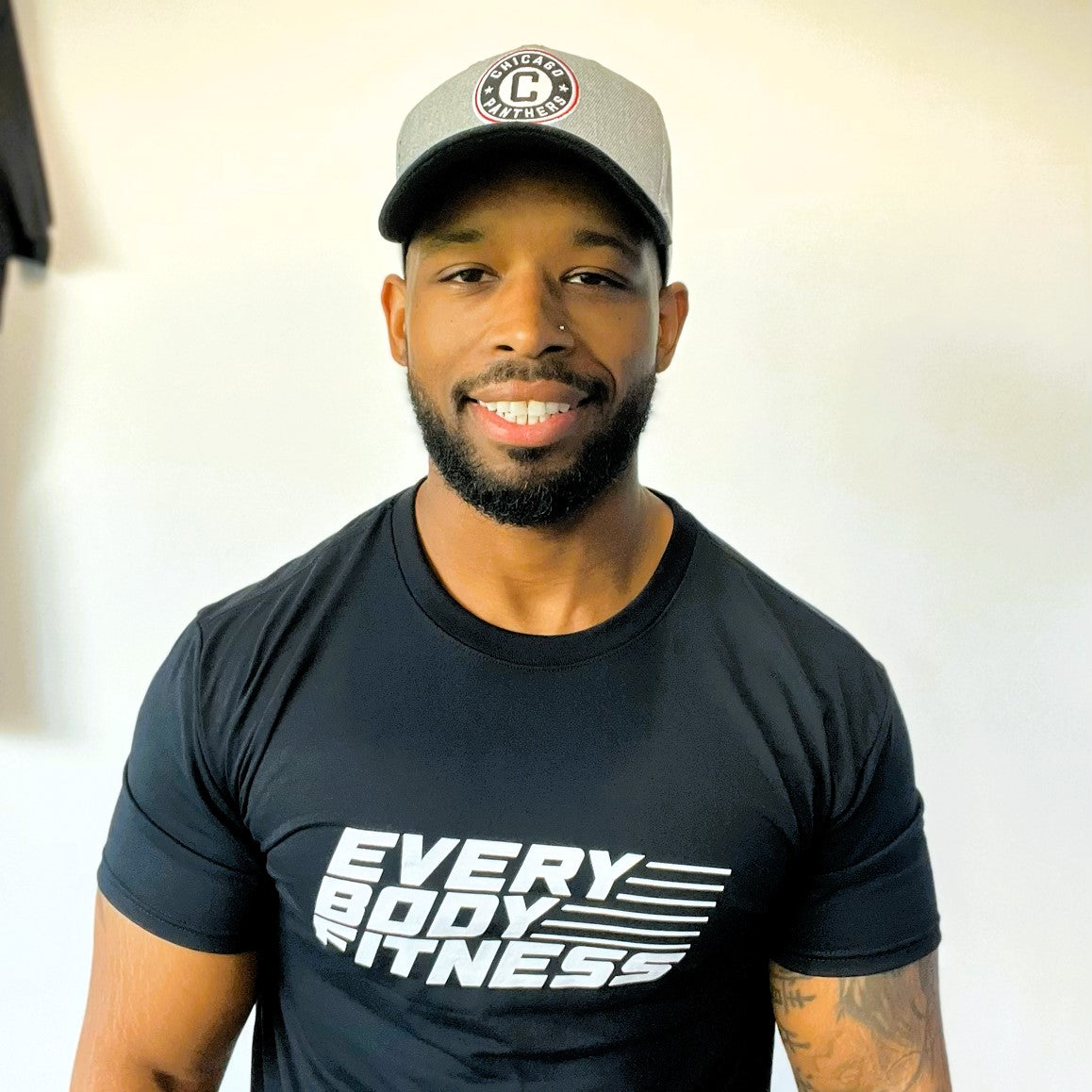 Man smiling at camera wearing sports cap and an EveryBody Fitness shirt.