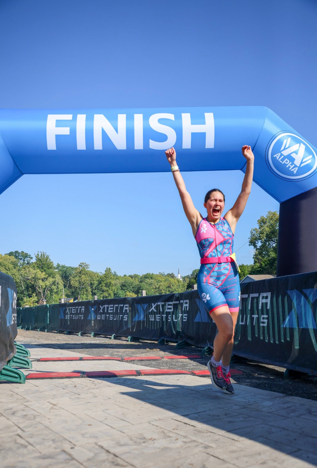 Woman crossing finishing line of race with arms raised in celebration.