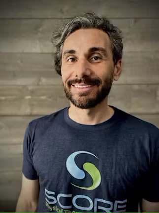 Man with beard smiling at camera and wearing SCORE t-shirt.