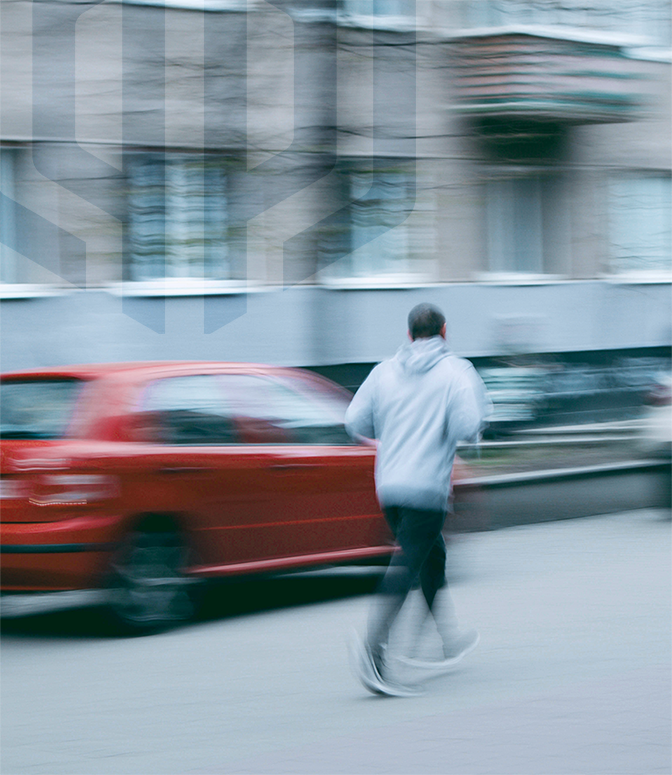 Man wearing hoodie jogging on city street passing parked red car.