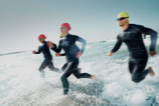 Four triathletes in wetsuits and swim caps running out of the ocean.