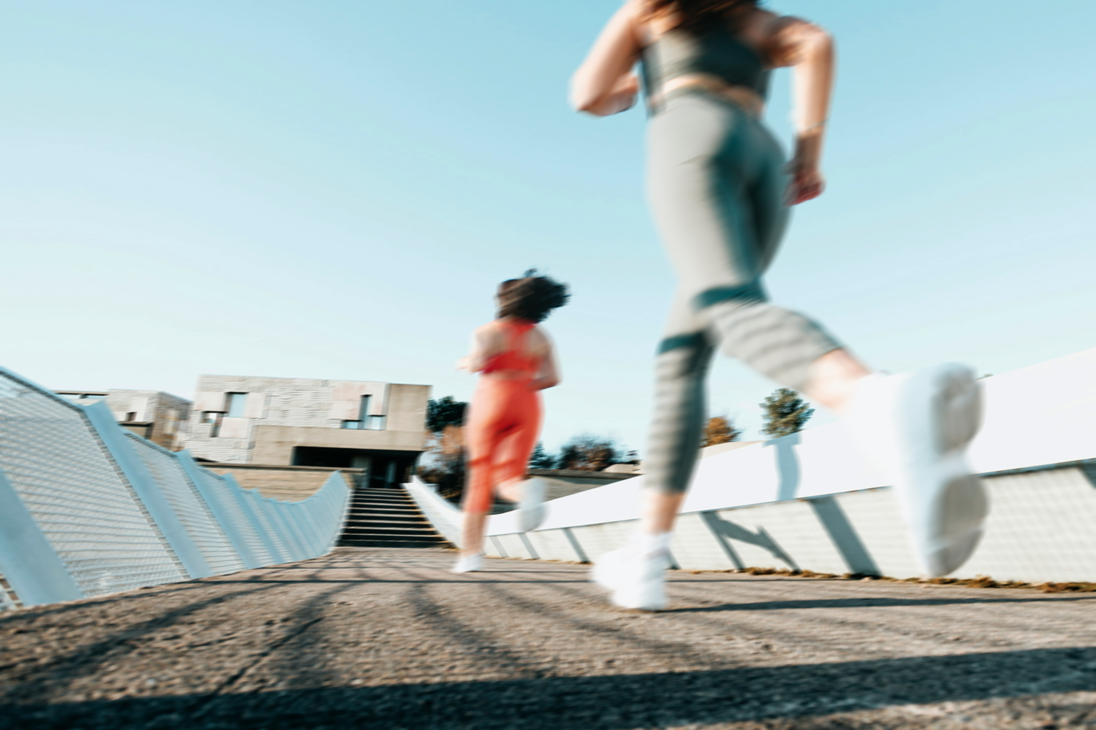 Two women in exercise clothes jogging across a bridge,