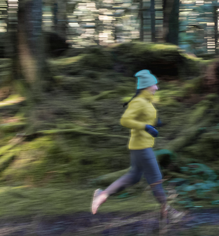 Woman in cold weather running gear jogging along a forest trail.