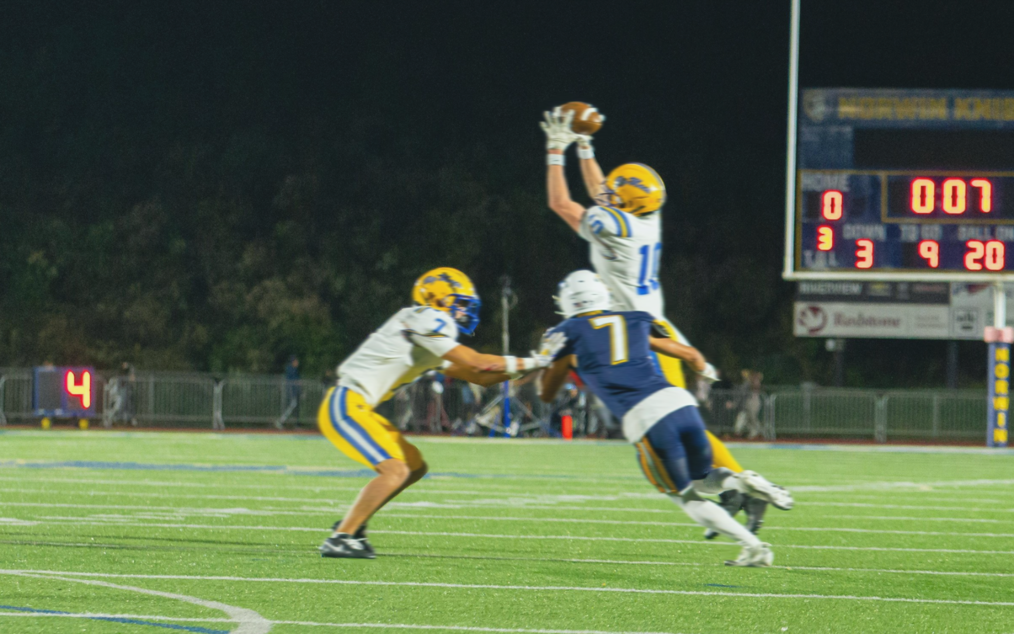 Two football players in action on a field with a scoreboard in the background.